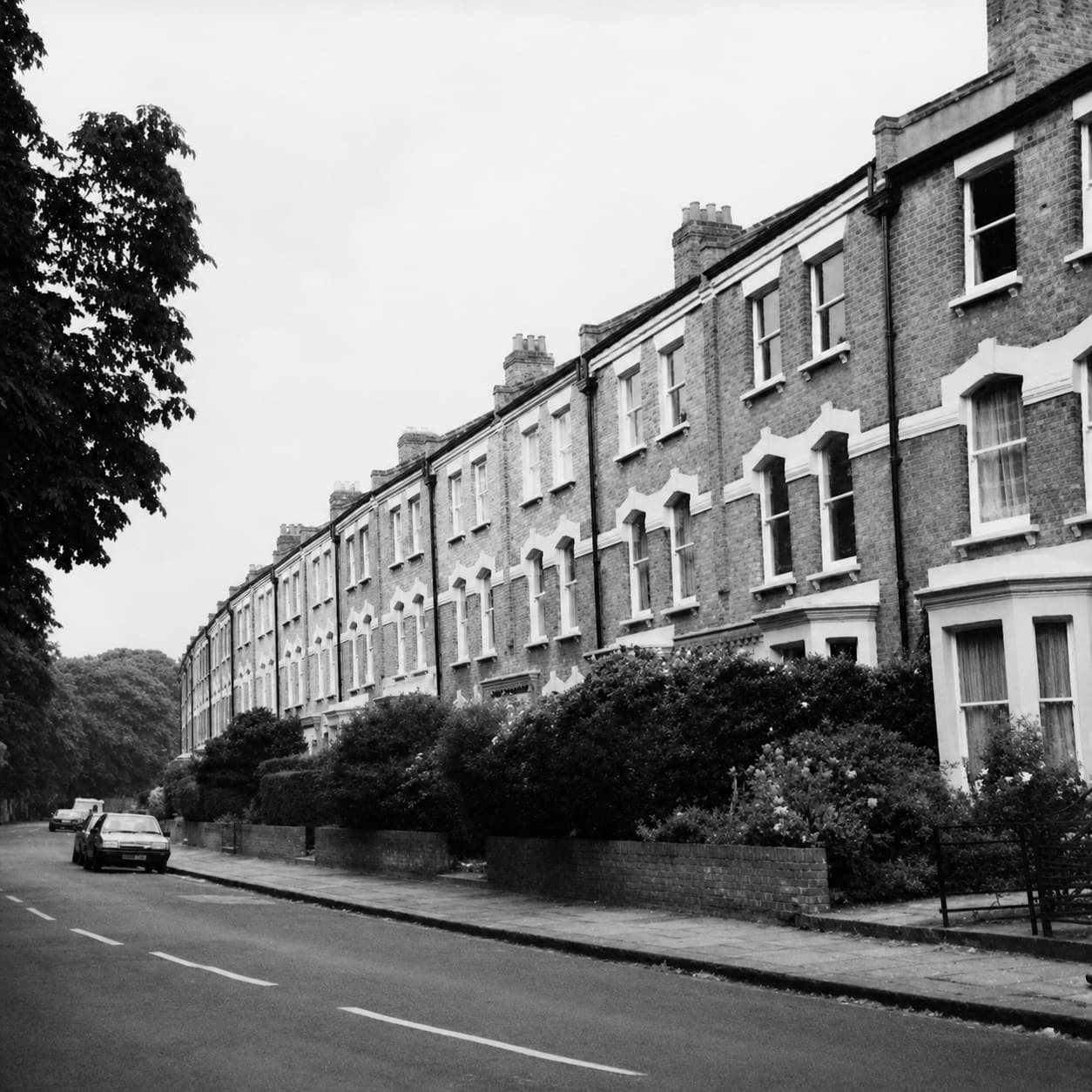 Black-and-white photograph of a curving Victorian terraced street in Hackney, photographed in the early 1980s, with mature trees and a single parked car visible.