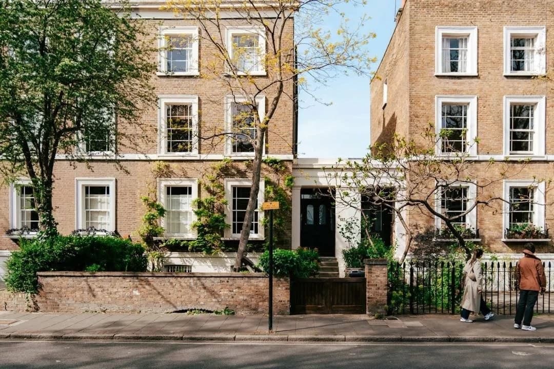 Restored Hackney terrace in spring sunlight, two figures walking past